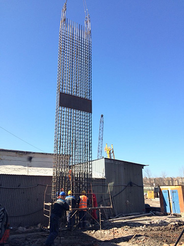 Процесс погружения арматурного каркаса в закладку стены в грунте